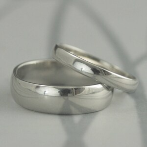 May include: Two silver wedding bands, one slightly larger than the other, are stacked on top of each other. The bands are smooth and shiny.