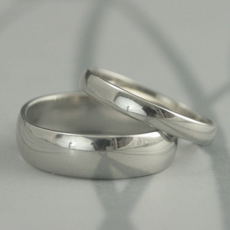 May include: Two silver wedding bands, one slightly larger than the other, are stacked on top of each other. The bands are smooth and shiny.