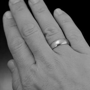 May include: A close-up of a hand wearing a simple silver wedding band.