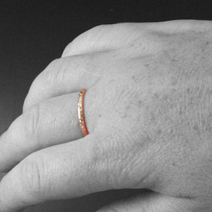 May include: A thin, rose gold band ring with a textured surface.