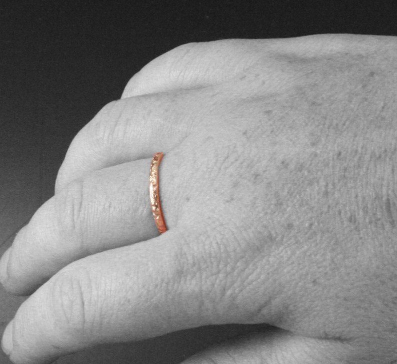 May include: A thin, rose gold band ring with a textured surface.