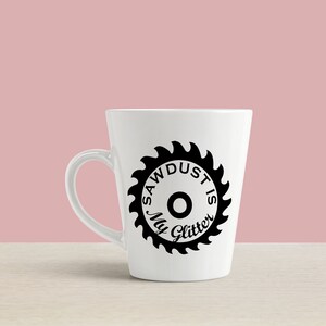 May include: White ceramic coffee mug with a black saw blade design and the text "Sawdust is my glitter".