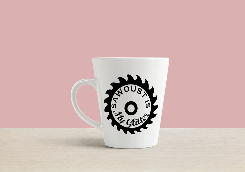 May include: White ceramic coffee mug with a black saw blade design and the text "Sawdust is my glitter".