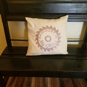May include: A black wooden bench with a white pillow featuring a pink glitter saw blade design with the text "Sawdust is Glitter".
