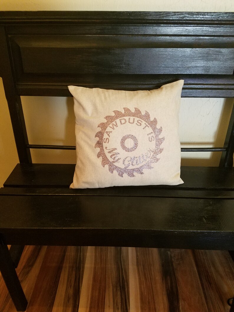 May include: A black wooden bench with a white pillow featuring a pink glitter saw blade design with the text "Sawdust is Glitter".