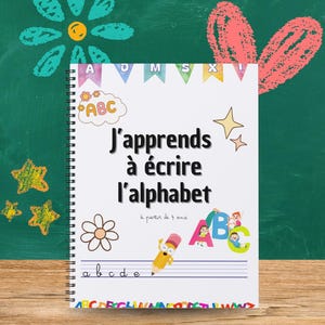 Peut inclure: Cahier à spirales avec le texte "J'apprends à écrire l'alphabet". La couverture présente des illustrations colorées de l'alphabet, des étoiles, un crayon et une fleur. Conçu pour les enfants à partir de 4 ans.