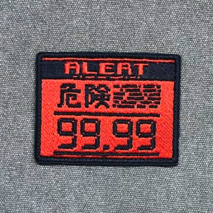 May include: A rectangular embroidered patch with a black border. The top section features the word ALERT in red text on a black background. The middle and bottom sections are red with black Japanese characters and the number 99.99 in black.