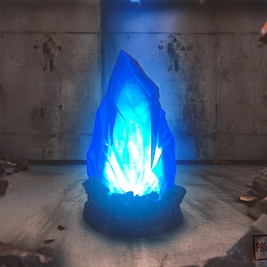 Könnte beinhalten: Eine leuchtende blaue Kristallskulptur mit einer gezackten, spitzen Form. Der Kristall strahlt ein helles weißes Licht von innen aus, das auf einem dunkelblauen Sockel steht. Der Hintergrund ist ein Betonraum mit Graffiti.