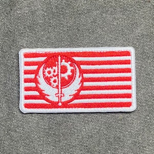 May include: A rectangular patch with a red and white striped design. The patch features a white emblem with a gear, wings, and a vertical line. The patch has a white border.