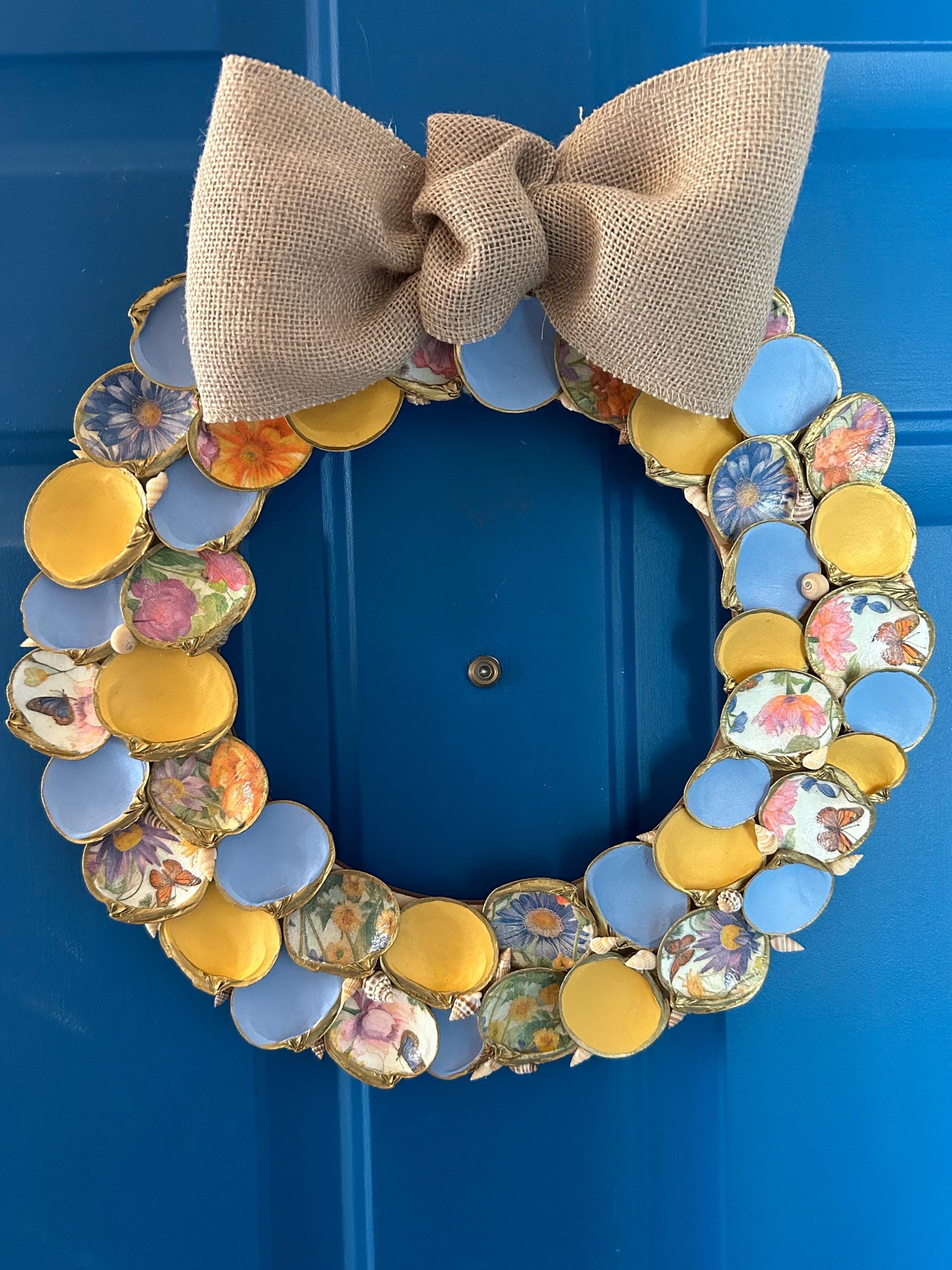 Kranz dekoriert mit gelb und blau bemalten Muscheln, floral geschöpften Muscheln die in Gold getrimmt sind & kleinen Akzentmuscheln.
