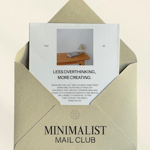 Op de afbeelding: Een beige envelop met een kaart erin. De kaart bevat de tekst "LESS OVERTHINKING, MORE CREATING." en "MINIMALIST MAIL CLUB." De kaart heeft ook een kleine afbeelding van een tafel met een lamp en een boek. De envelop heeft de tekst "THE GOOD CRAFT".