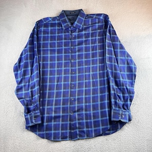 May include: A long-sleeved button-down shirt in a blue plaid pattern. The shirt features a classic collar and buttoned cuffs. The plaid design incorporates shades of blue and gray, creating a visually appealing pattern. The shirt is made of a smooth fabric.