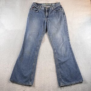 May include: Light blue denim jeans with a flared leg design. The jeans have a classic five-pocket style, a button and zipper closure, and belt loops. The jeans are pre-worn and have some discoloration.