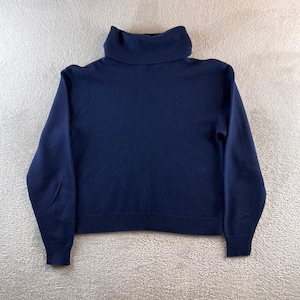 May include: A solid navy blue long-sleeve sweater featuring a high turtleneck collar, long sleeves with ribbed cuffs, and a ribbed hemline. The garment is constructed from a knit fabric with a smooth, consistent texture throughout the entire piece.