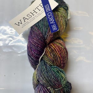 May include: A skein of worsted weight yarn in a variegated colorway of purple, green, and yellow. A white tag attached to the yarn reads WASHTE, 210 yd, 100 g, 18 sts, US 7-9 OR 4.5-5.5 mm, 100% Superwash. A blue tag reads 866 ARCO IRIS.