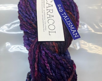 Puede incluir: Una madeja de hilo super bulky Caracol en el color 249 Talisman, con una mezcla variada de tonos morado intenso, azul y rojo anaranjado. La etiqueta indica 87 metros, 150 gramos y una composición de 100% lana merino superwash.