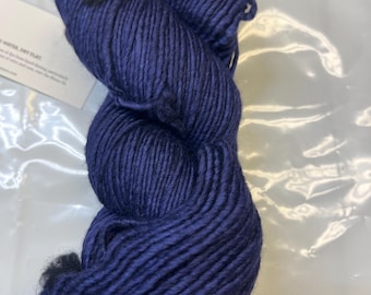 May include: A skein of deep blue yarn with black flecks. The yarn is wound into a ball shape and is ready for knitting or crocheting.