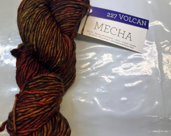 May include: A skein of "Mecha" yarn in shades of brown, orange, and yellow. The yarn is labeled "227 Volcan". The yarn is made of Superwash Merino Wool. The label also includes the approximate yardage and weight of the yarn.