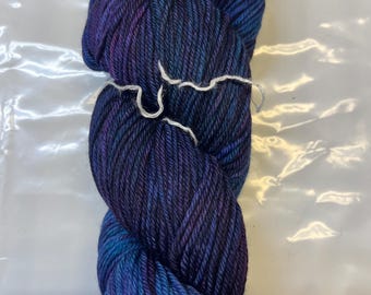 May include: A skein of deep blue yarn with purple and teal color variations. The yarn is wound into a ball shape and is ready for knitting or crocheting.