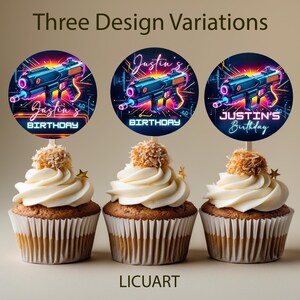 May include: Three cupcakes with white frosting, topped with a coconut ball and a star. Each cupcake has a circular topper with a neon blue and pink laser gun design and the text "Justin's Birthday".