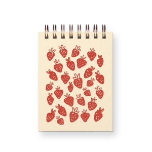 May include: A spiral-bound notebook with a cream-colored cover featuring a repeating pattern of small, hand-drawn red strawberries. The wire binding is located at the top of the rectangular notebook, which displays a consistent strawberry print.