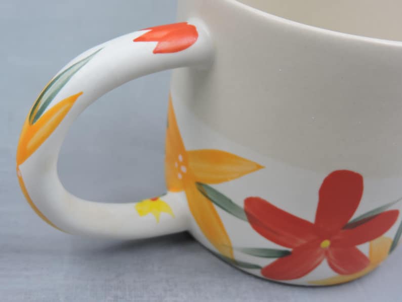 Puede incluir: Taza de cer&aacute;mica color crema con un asa grande, adornada con dise&ntilde;os florales pintados a mano en naranja, rojo y amarillo, con hojas verdes. Una pieza decorativa y alegre para disfrutar de bebidas.