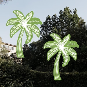 Puede incluir: Dos pegatinas de palmeras verdes con contornos blancos. La pegatina de la izquierda dice "aurora" y la pegatina de la derecha dice "elena".