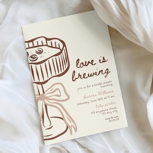以下が含まれることがあります： クリーム色の招待状。茶色のケーキとリボンのイラスト。テキスト「love is brewing」は茶色の筆記体で書かれています。追加のテキストには、ブライダルシャワーのイベント詳細が含まれています。