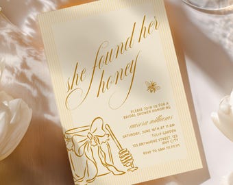 May include: A rectangular bridal shower invitation card with a pale yellow striped background and gold text. The card features the phrase "she found her honey," a small bee illustration, and a line drawing of a honey jar with a dipper.