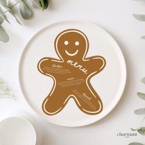 Op de afbeelding: Een witte keramische plaat met een bruin peperkoekmannetje menudesign. Het menu bevat secties voor voorgerecht, hoofdgerecht en dessert. De tekst is in handschrift. De plaat is omgeven door groen.