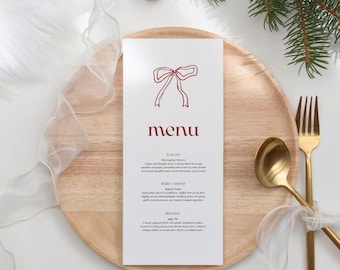 Op de afbeelding: Een witte menukaart met een rode strik illustratie en het woord "menu" in het rood. Het menu staat op een houten bord, met een gouden vork en lepel. Een dennenappel en groen zijn op de achtergrond.