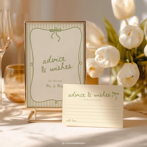 Könnte beinhalten: Ein goldgerahmtes Schild und eine passende Karte mit dem Text "advice & wishes" in grüner Schrift. Das Schild hat einen gestreiften Hintergrund und einen dekorativen Rahmen. Die Karte hat Linien zum Schreiben und den Text "for the new Mr. & Mrs."