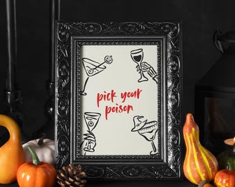 May include: A framed print with the text "pick your poison" in red script. The print features line drawings of cocktail glasses with Halloween-themed elements. The frame is black and ornate, with pumpkins and gourds in the foreground.