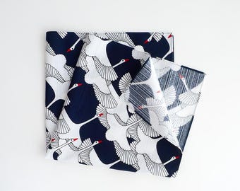 May include: Folded navy blue and white fabric with a repeating pattern of flying white birds with red beaks. The fabric is folded in a square shape, with a portion of the fabric unfolded to reveal the pattern.