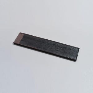 May include: A long, rectangular black ceramic tray with a subtle textured surface. The tray has a thin, light pink border.