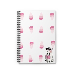 Puede incluir: Una libreta espiral blanca con un patrón de maíz dulce rosa y blanco y un fantasma leyendo un libro. El fantasma tiene el nombre "Emily" escrito encima.