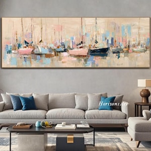 May include: Abstract painting of sailboats in a harbor, with a neutral background and a gold frame. The artwork features a palette of pink, blue, and beige, creating a serene and nautical theme. The painting is displayed above a gray sofa.