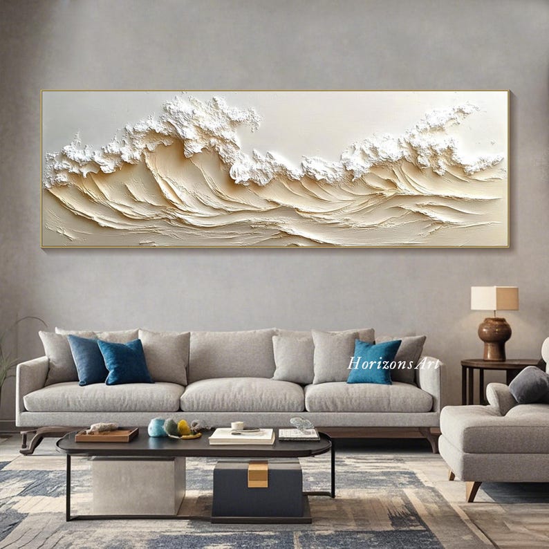 May include: A large abstract painting of white waves on a beige background. The painting is framed in a thin gold frame and hangs on a wall above a gray sofa.