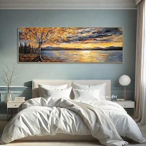 May include: A painting of a lake scene with a tree in the foreground and a sunset in the background. The painting is done in a palette of warm colors, including yellow, orange, and red. The painting is displayed on a wall above a white bed with white bedding.