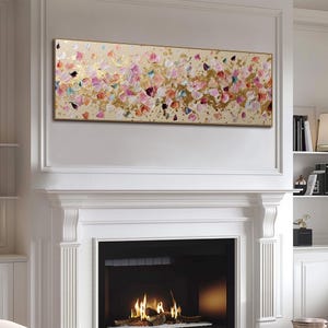 May include: A rectangular abstract painting with a gold frame. The artwork features a beige background with colorful brushstrokes in pink, purple, gold, and blue. The painting is mounted above a white fireplace.
