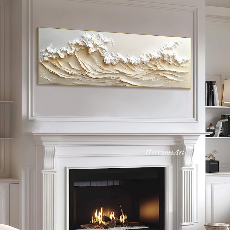 May include: A white and gold textured wall art piece depicting a wave crashing. The art is framed in a thin gold frame and is hanging above a white fireplace.
