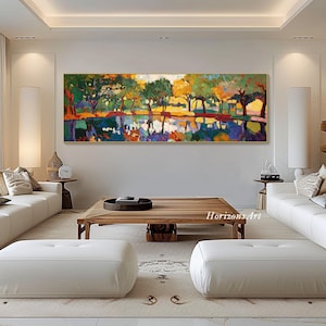 May include: A colorful abstract painting of a landscape with trees reflected in a still body of water. The painting is framed in gold and hangs on a white wall in a living room setting.