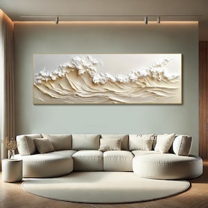 May include: A large abstract painting of white waves on a beige background. The painting is framed in a thin gold frame and is hanging on a wall in a living room.