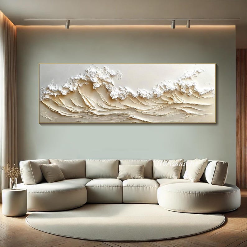 May include: A large abstract painting of white waves on a beige background. The painting is framed in a thin gold frame and is hanging on a wall in a living room.