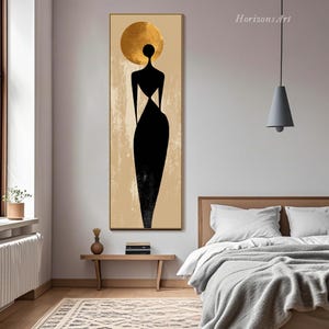 Puede incluir: Impresi&oacute;n art&iacute;stica abstracta que presenta una silueta negra de una figura con un halo dorado en forma de sol sobre un fondo beige. La obra de arte est&aacute; enmarcada en dorado y se exhibe en un dormitorio.