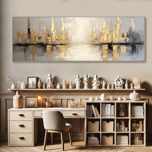 Puede incluir: Pintura abstracta de paisaje urbano en tonos dorados y grises. La pintura representa un horizonte urbano con edificios reflejados en el agua. La pintura est&aacute; enmarcada y colgada en una pared sobre un escritorio.
