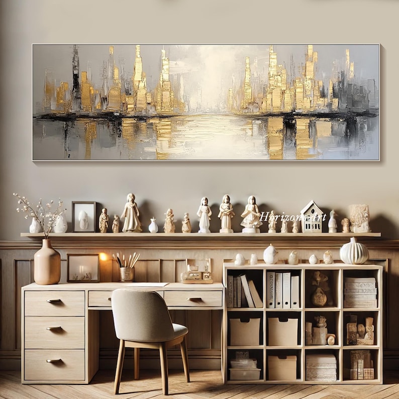 Puede incluir: Pintura abstracta de paisaje urbano en tonos dorados y grises. La pintura representa un horizonte urbano con edificios reflejados en el agua. La pintura est&aacute; enmarcada y colgada en una pared sobre un escritorio.