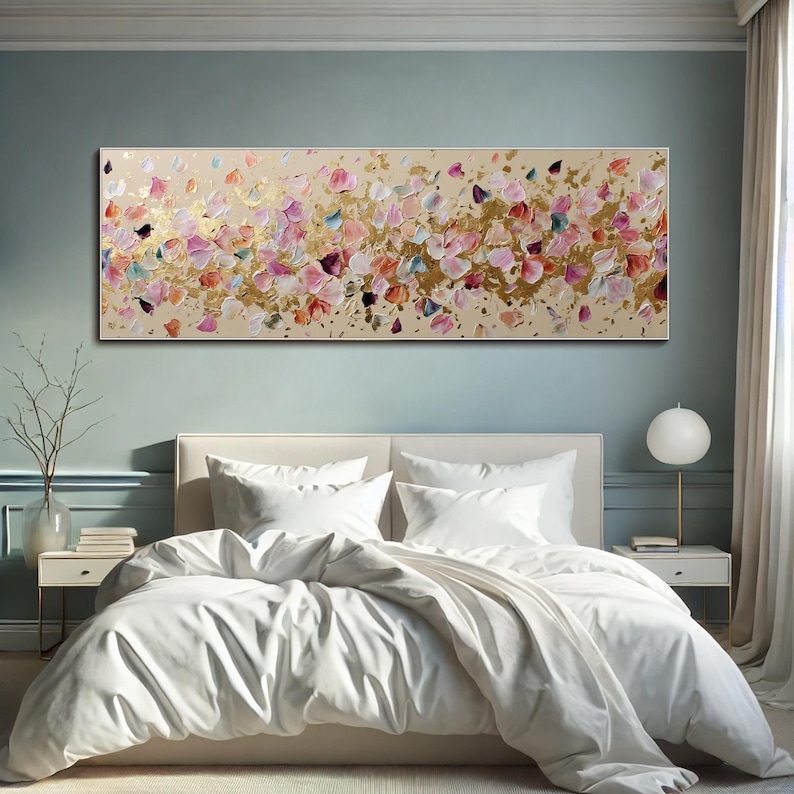 May include: A long, rectangular abstract painting with a beige background. The artwork features textured brushstrokes in shades of pink, gold, and blue. The painting is mounted above a bed with white bedding.