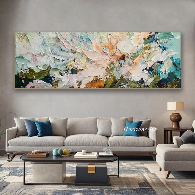 May include: Abstract painting with a gold frame, featuring a colorful, textured design with shades of blue, green, pink, and white. The painting is displayed on a wall above a gray sofa and a coffee table.