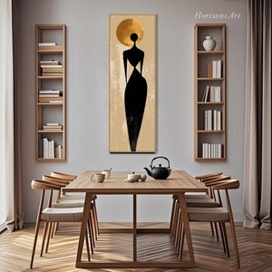 Puede incluir: Una impresi&oacute;n art&iacute;stica abstracta que presenta una figura negra con un halo dorado sobre un fondo beige, enmarcada en dorado. La obra de arte cuelga sobre una mesa de comedor de madera con sillas, una tetera y tazas. El texto "Horizons Art" es visible en la esquina superior derecha.